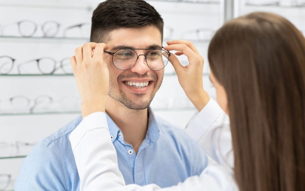Це зображення чоловіка, який приміряє нові окуляри у магазині Оптика про. Він уважно дивиться на дзеркало, щоб переконатися, що окуляри ідеально підходять його обличчю. Чоловік може бути задоволений вибором нових окулярів, що підходять до його особистого стилю та забезпечують гарний зоровий комфорт.